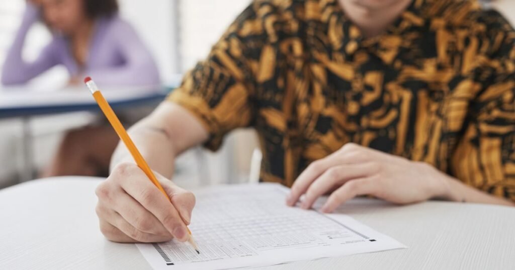 Student writing a polytechnic English question paper in an exam hall